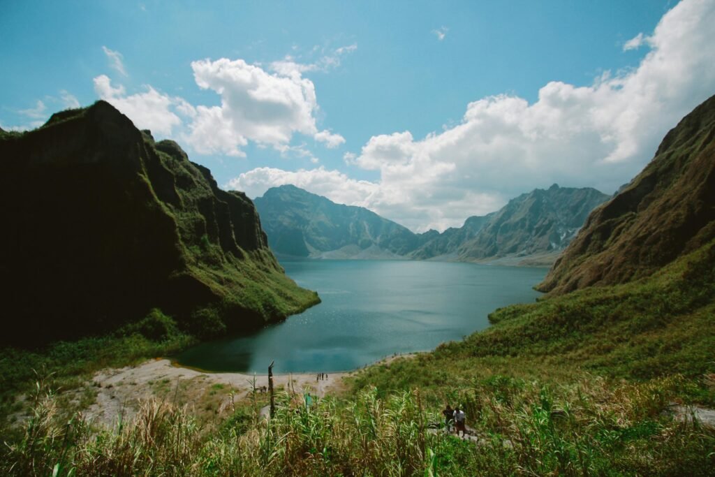 A tranquil scene of Crater Lake at Mount Pinatubo, surrounded by lush mountains and a clear blue sky.